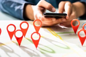 A person using a smartphone with a map in the background marked by red location pins, symbolising local SEO effort and cost.