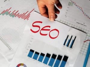 A man is holding a paper with the word SEO and bar graphs indicating high performance and SEO marketing cost