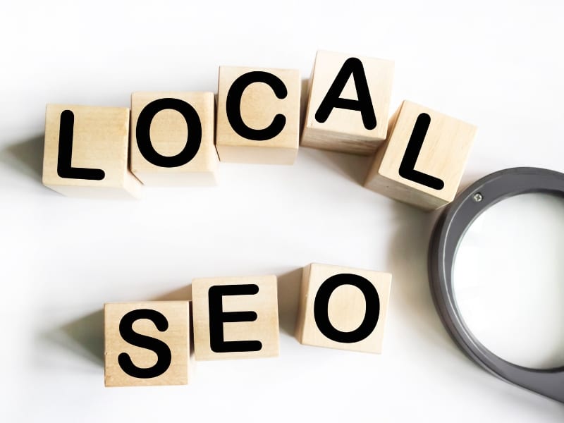 Wooden blocks spelling local SEO with magnifying glass showing concept of seo marketing package