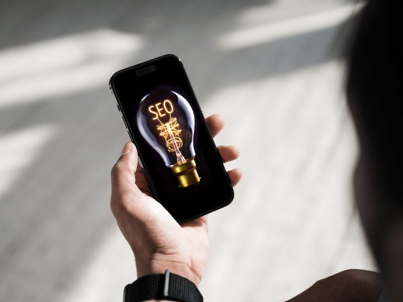 Mobile seo optimisation concept shown on smartphone displaying SEO lightbulb graphic held in hand.
