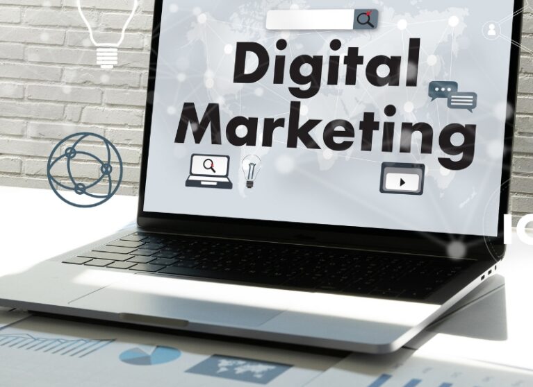 Laptop screen displaying bold "Digital Marketing" text surrounded by online icons on a office desk setup.