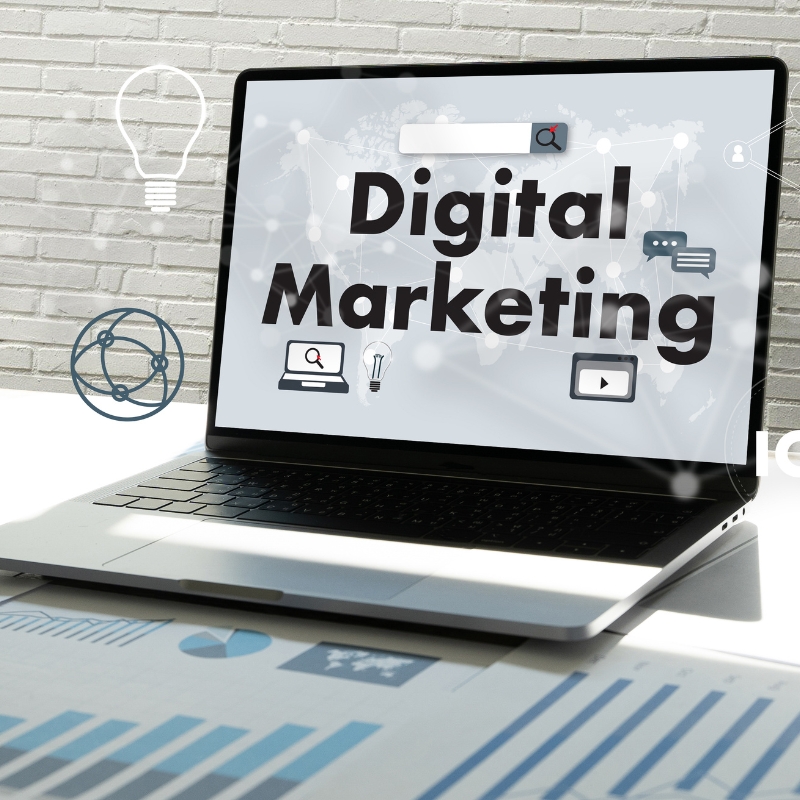 Laptop screen displaying bold "Digital Marketing" text surrounded by online icons on a office desk setup.